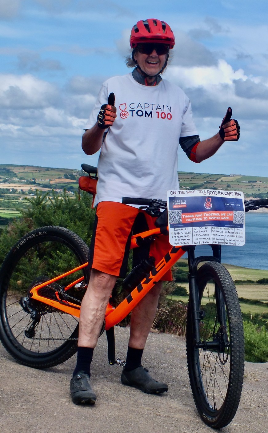 Rob in a Captain Tom 100 t-shirt with the orange Trek mountain bike on a hill overlooking the North Yorkshire coast near Ravenscar.